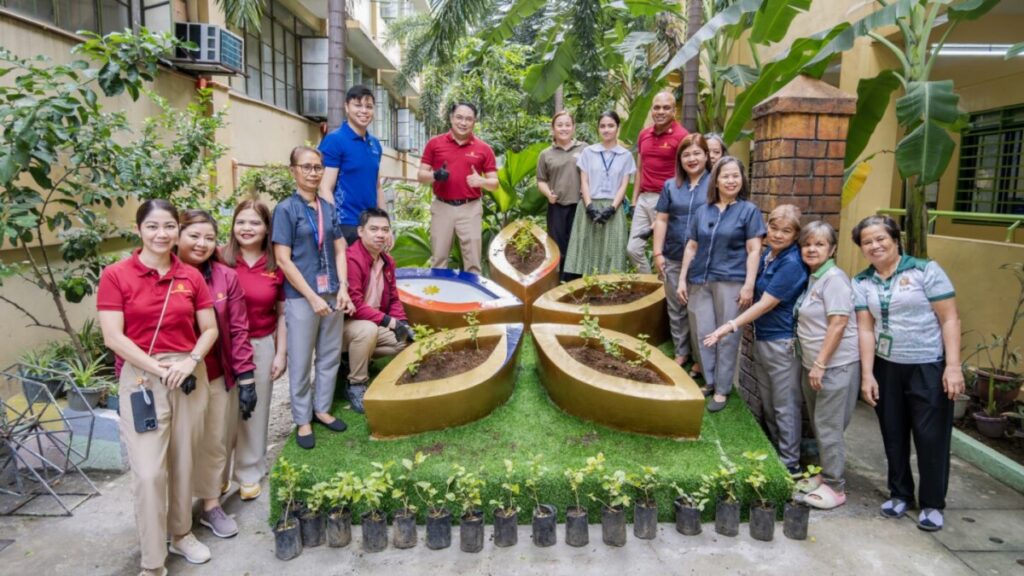 Volunteers in red shirts and teachers around a flower-shaped planting display at Tambo Elementary School