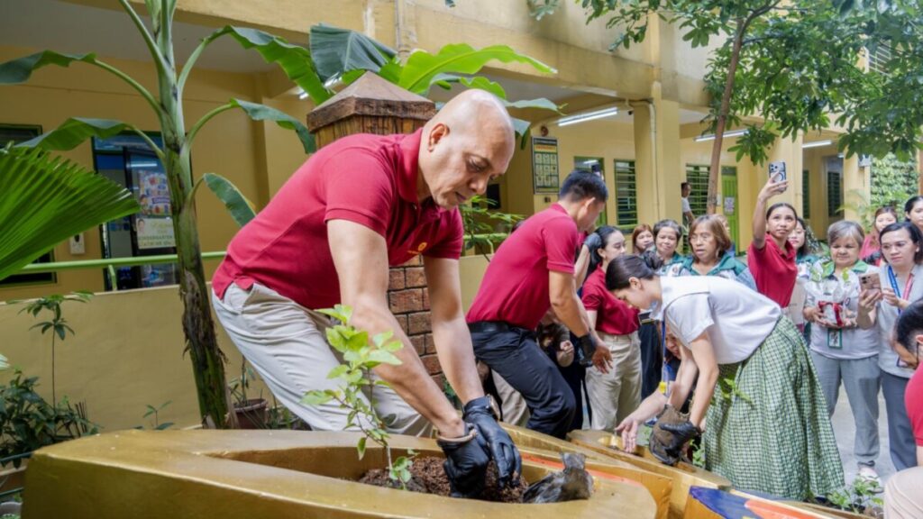 A volunteer planting sampaguita while students and teachers look on